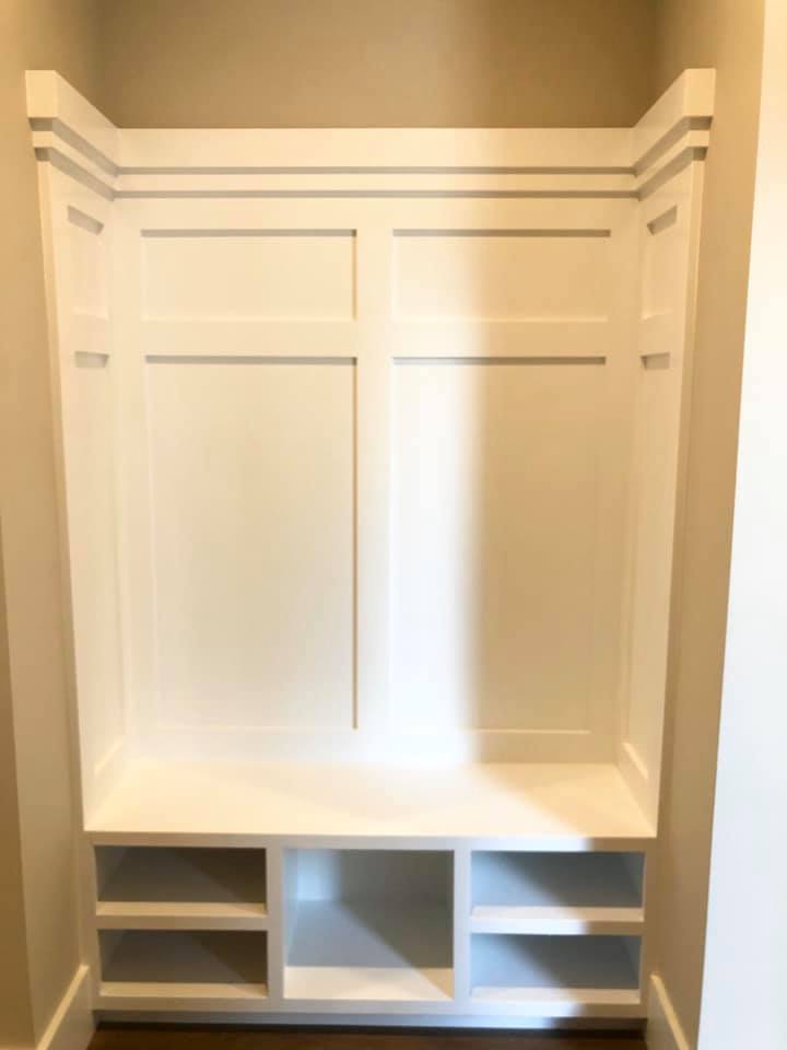 White built-in locker unit with panelled back, stepped cornice, a bench seat and open cubbies beneath.